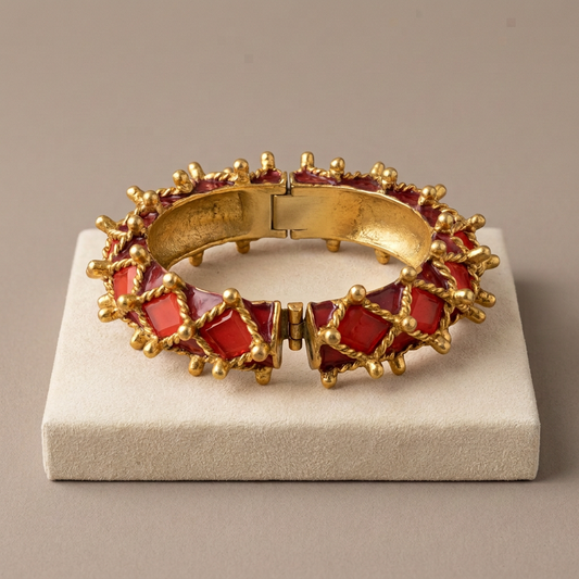 AI-styled editorial display of Kenneth Jay Lane coral and gold spiked cuff on an ivory plinth